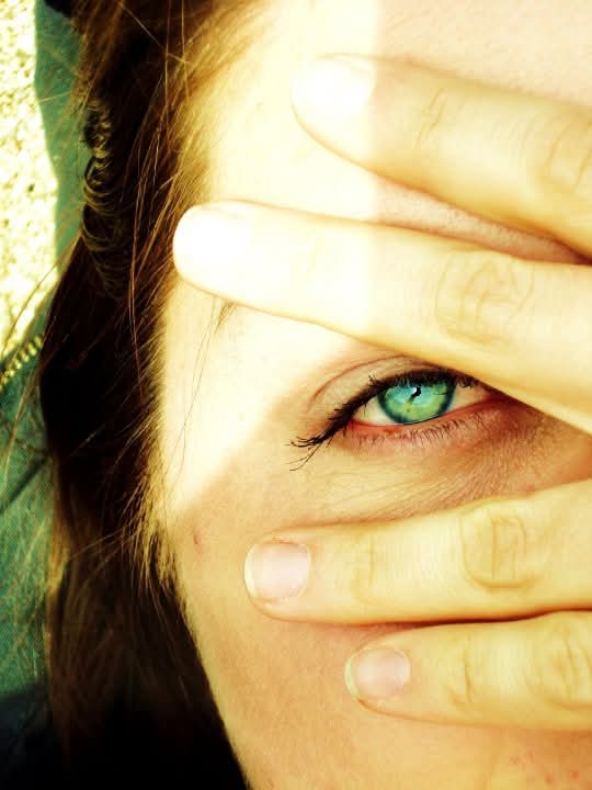 Extreme close-up of a woman's eye, seen between her fingers