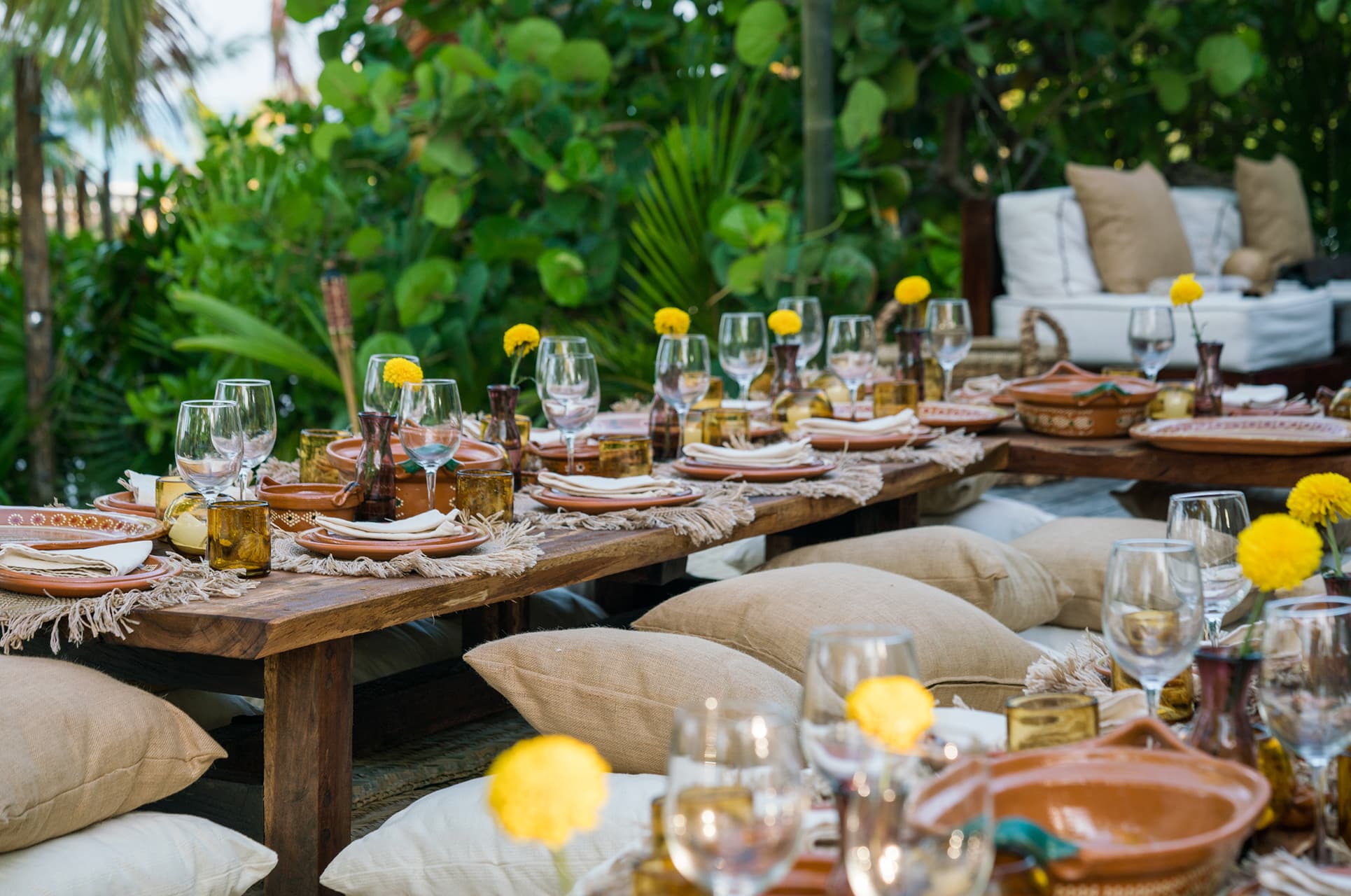 A long boho dinner table set outdoors among tropical greenery
